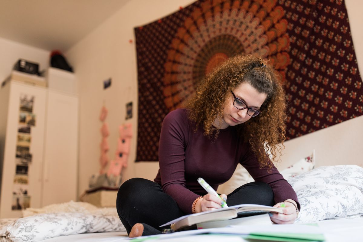 zur Vergrößerungsansicht des Bildes: Studentin sitzt auf ihrem Bett und lernt.