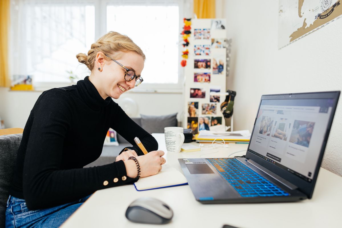 zur Vergrößerungsansicht des Bildes: Frau sitzt zu Hause am Laptop und macht sich Notizen, Foto: Christian Hüller