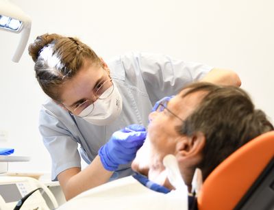 Studentin mit Mundschutz behandelt Patienten in der Zahnklinik, Foto: Anton Stolle