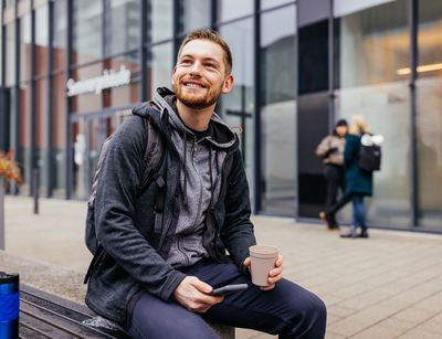Studienbotschafter Michael sitzt auf einer Bank auf dem Campus und trinkt Kaffee, Foto: Christian Hüller