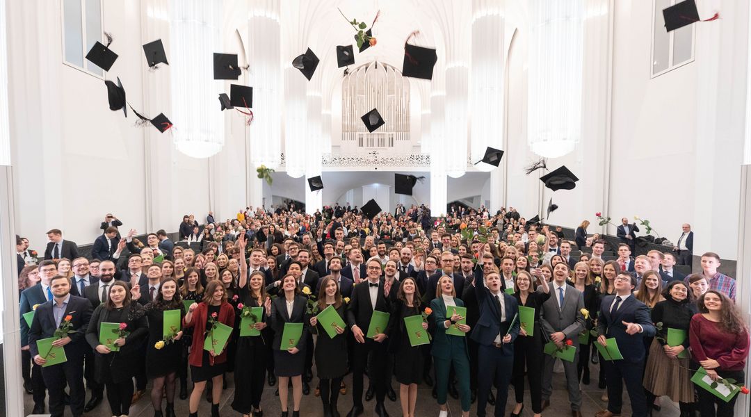 Die Absolventen und Absolventinnen stehen zum Gruppenfoto zusammen und schmeißen ihre schwarzen Hüte in die Luft, Foto: Christian Hüller