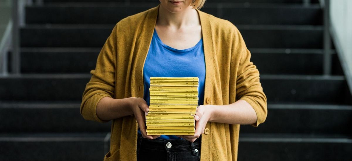 Studentin hält gelben Bücherstapel vor sich und blickt darauf, Foto: Christian Hüller