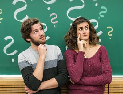 Ein Student und eine Studentin stehen vor einer Tafel mit angezeichneten Fragezeichen, Foto: Christian Hüller