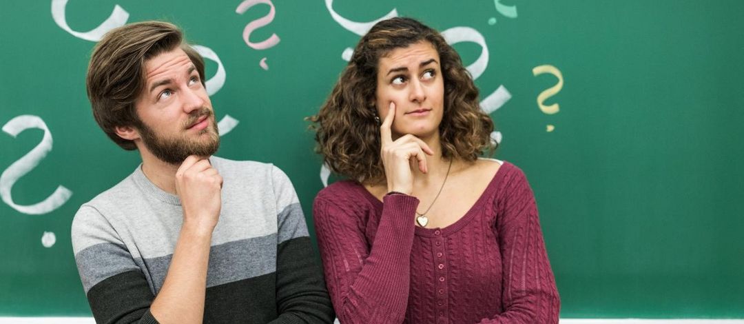 Ein Student und eine Studentin stehen vor einer Tafel mit angezeichneten Fragezeichen, Foto: Christian Hüller
