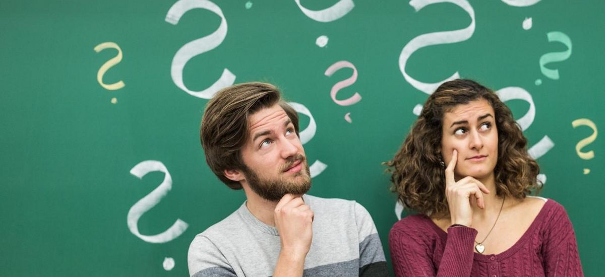 Ein Student und eine Studentin stehen vor einer Tafel mit angezeichneten Fragezeichen, Foto: Christian Hüller