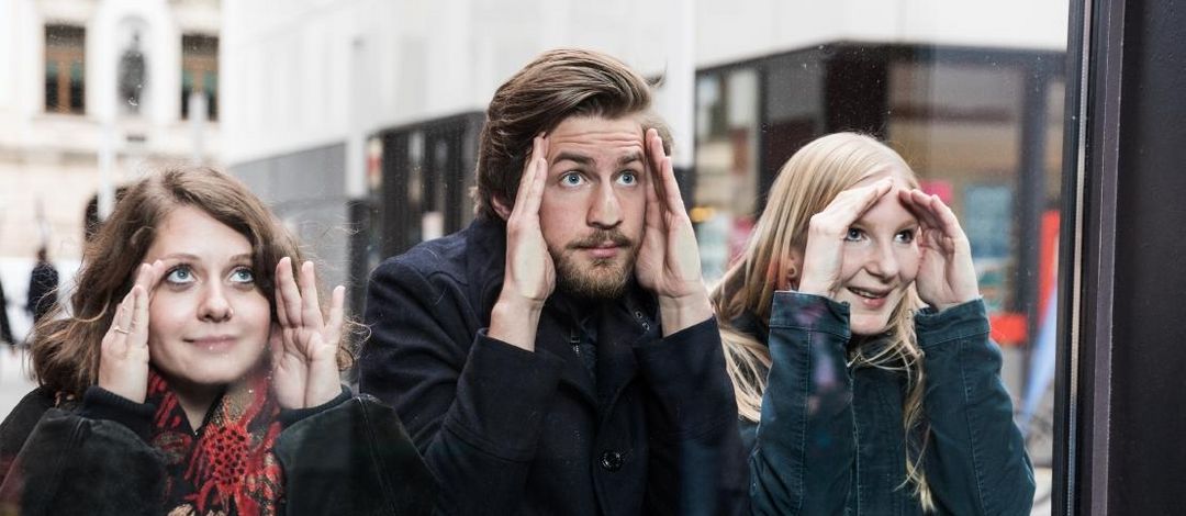 Foto von drei Studierenden die durch ein Fenster in das Hörsaalgebäude gucken