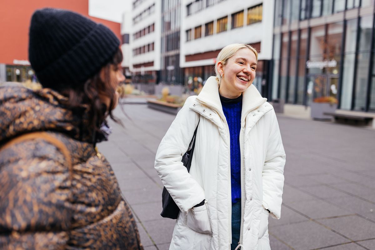 Studienbotschafterin Vivi steht auf dem Campus und lacht mit einer Studentin, Foto: Christian Hüller