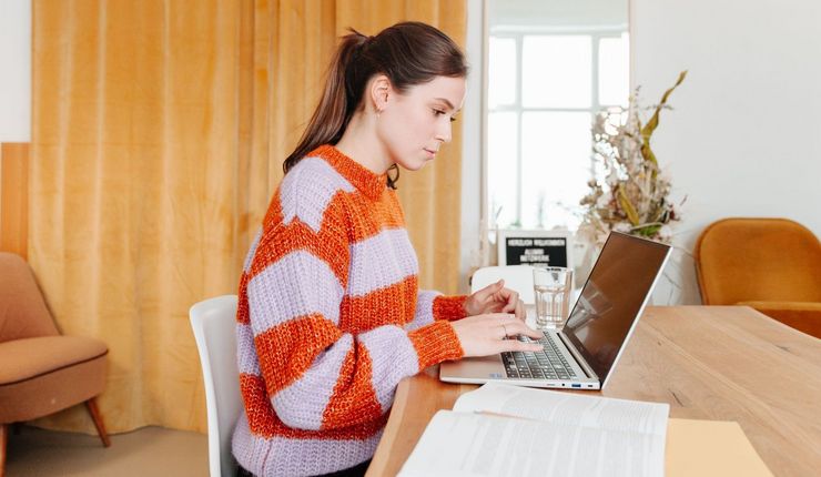 Junge Frau sitzt am Schreibtisch, vor ihr steht ein aufgeklappter Laptop, Foto: Grit Hartung