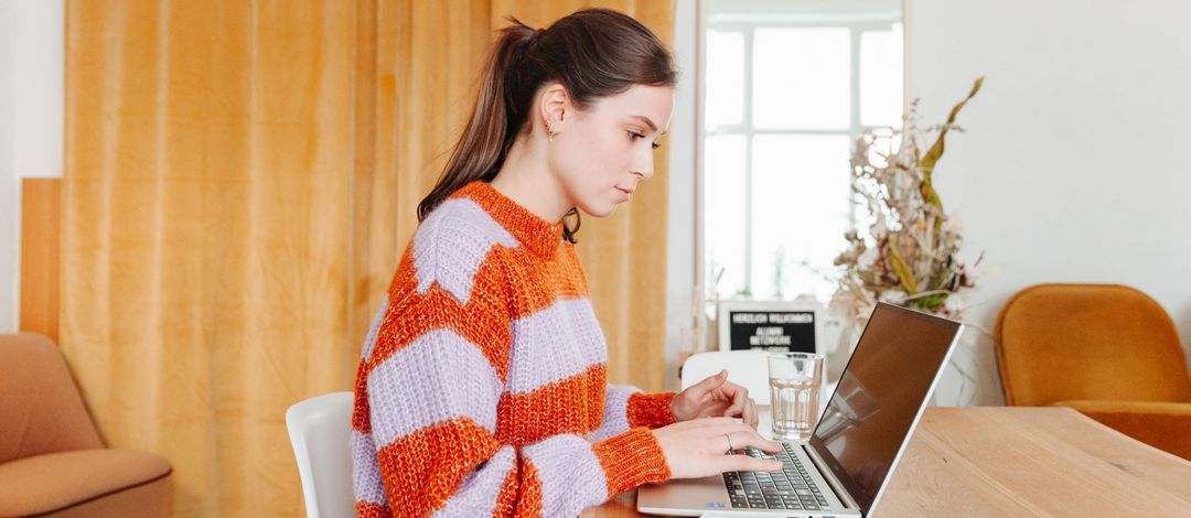 Junge Frau sitzt am Schreibtisch, vor ihr steht ein aufgeklappter Laptop, Foto: Grit Hartung