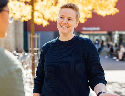 Studienbotschafterin Sara im Gespräch auf dem herbtlichen Campus, die Sonne scheint im Hintergrund, Foto: Christian Hüller