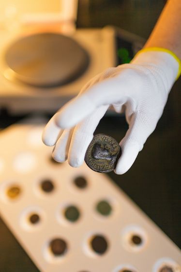 Nahaufnahme auf eine antike Münze, die mit Handschuhe gehalten wird, Foto: Christian Hüller