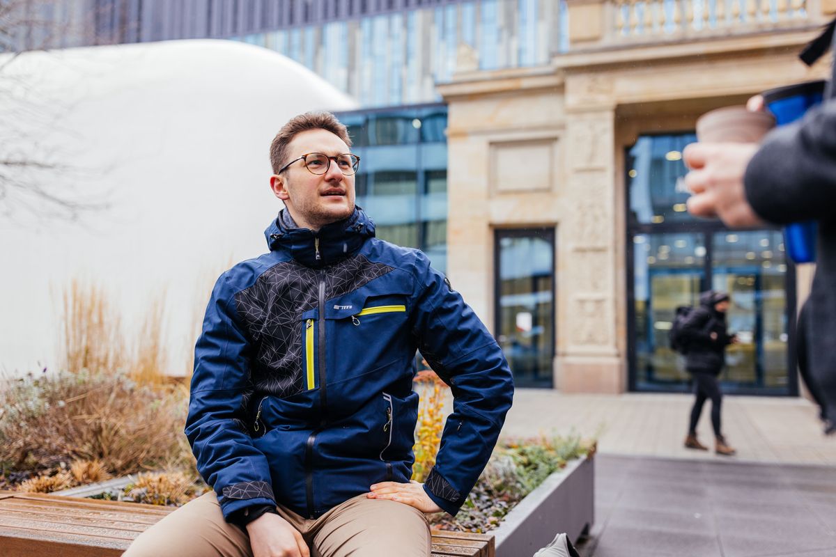 Studienbotschafter Sebastian sitzt auf dem Campus und spricht mit einem Studenten, Foto: Christian Hüller