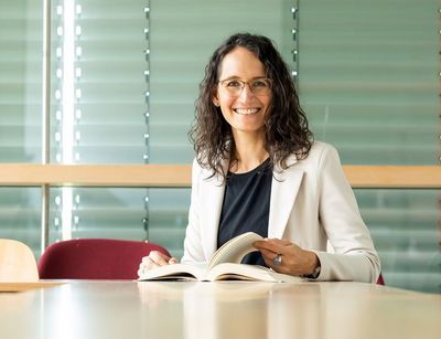 Prof. Dr. Miriam Nandi mit aufgeschlagenen Buch am Tisch, Foto: Swen Reichhold