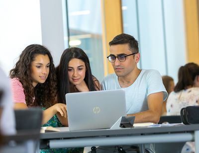 Symbolbild: Drei Studierende arbeiten gemeinsam an einem Laptop.