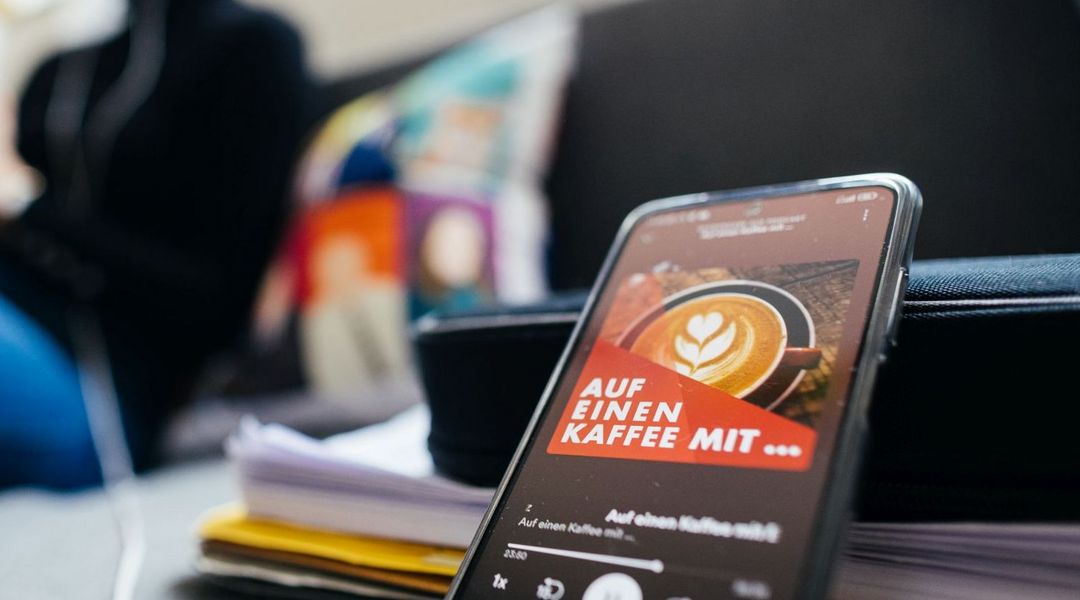 Frau sitzt auf dem Sofa und hört Podcast