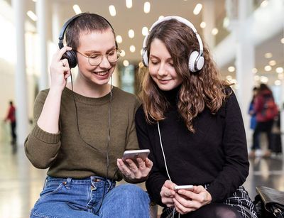 Zwei Studentinnen mit großen Kopfhörern hören in Neuen Augusteum der Uni Leipzig den neuen Podcast "Auf einen Kaffee mit...", Foto: Christian Hüller