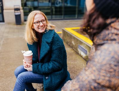 Studienbotschafterin Patricia sitzt auf einer Bank auf dem Campus und hält einen Becher in der Hand, Foto: Christian Hüller