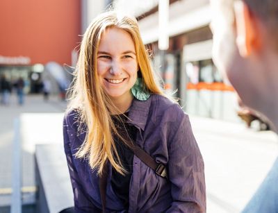 Studienbotschafterin Natalie lächelt beim Gespräch auf dem Campus, die Sonne scheint im Hintergrund, Foto: Christian Hüller