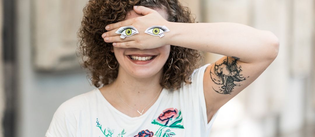 Studentin mit Hand vor dem Gesicht mit aufgeklebten Augen auf der Hand, Foto: Christian Hüller