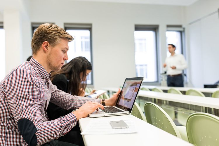 Student der Wirtschaftswissenschaften blickt auf seinen Laptop und notiert etwas im Seminar, Foto: Christian Hüller