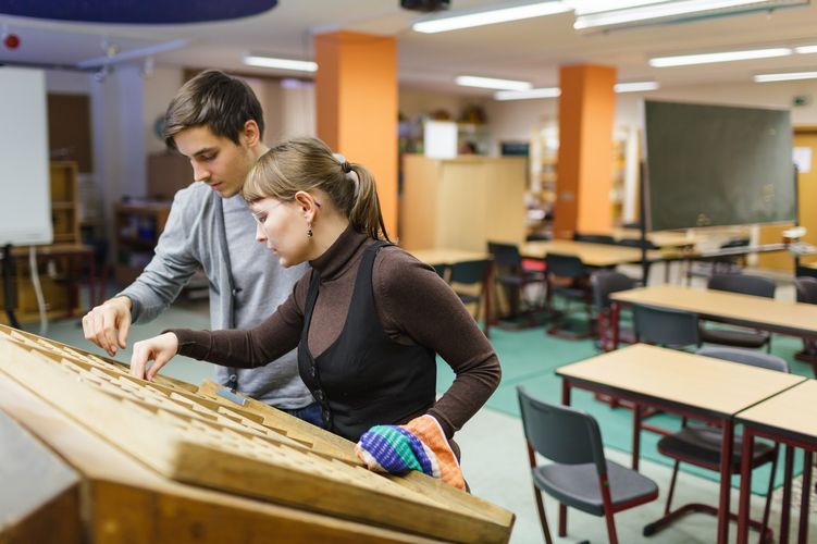 Zwei Studierende stehen vor einem schräg aufgestellten Brett. Im Hintergrund sieht man ein Klassenzimmer, Foto: Christian Hüller