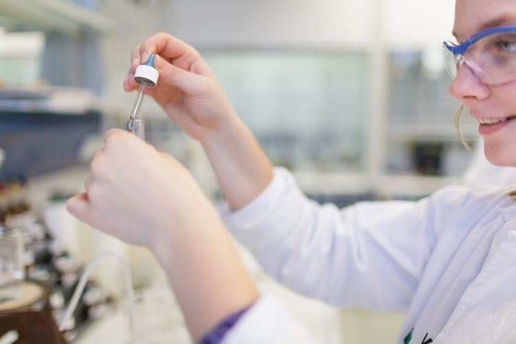 Studentin mit weißen Kittel und Schutzbrille fügt einen Stoff mittels Pipette in ein Reagenzglas ein, Foto: Christian Hüller