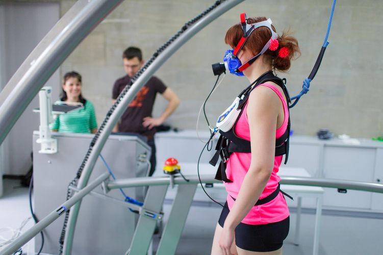 Eine verkabelte Probantin steht auf einem Laufband und im Hintergrund stehen Forscher*innen, Foto: Christian Hüller